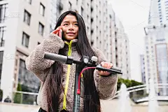 漂亮的亚洲年轻女孩讲她的电话，而骑电动车在大城市
