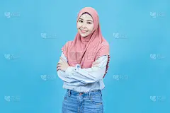 年轻美丽的亚洲穆斯林妇女的肖像在传统服装交叉双臂和微笑孤立在蓝色的背景