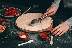 一个白人小女孩的手用一把圆刀切圣诞树——切菜板上的披萨面团像月亮一样薄