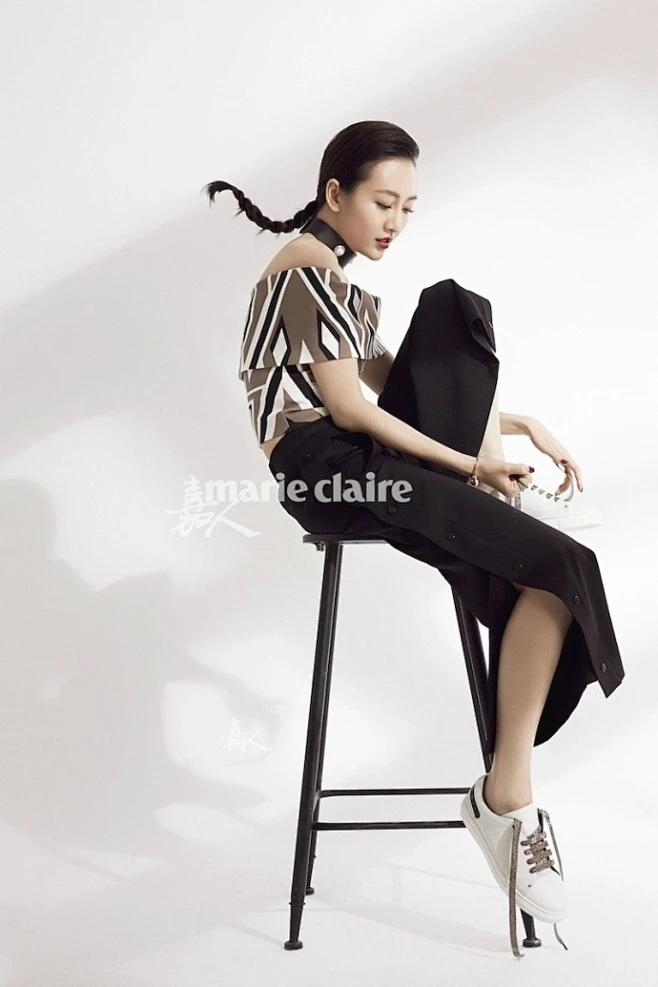 穿着几何图案的一字肩上衣黑色阔腿裤,搭配一双小白鞋,坐在高脚椅上