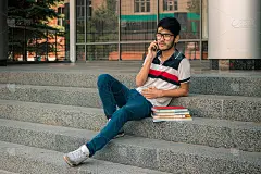年轻的学生坐在楼梯上拿着书和电话费