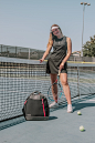 其中可能包括：a woman standing on a tennis court holding a racquet next to a bag