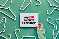 白色塑料衣架，手里拿着白纸。短信对快时尚说不。俯视图平铺在时尚的柔和绿色薄荷背景上。让快时尚慢下来，