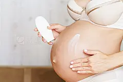 Pregnant woman aplying cream at her belly for prevention of stretch marks on the skin