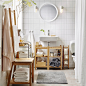 A medium size white bathroom with toilet roll stand, shelves and towel rack chair, all in bamboo.