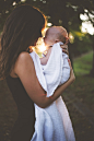 woman holding baby standing on field under tree during daytime