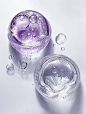 Two glass skincare products, one purple and the other white, filled with transparent water. Bubbles float on the liquid, creating a sense of overall transparency. White background, top view, high-definition photography, product photography