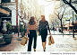 Rear view of two friends walking on the city street with shopping bags. Female shoppers carrying shopping bags while walking along the road.