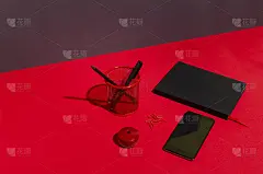 黑色的空白屏幕上的手机，笔记本，笔筒，铅笔，钢笔，卷笔刀在红色的桌子上，靠在黑暗的墙壁上