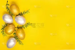 银的和金的鸡蛋，绿色的树枝从图像的左边边缘在一个普通的黄色背景。复活节卡片。Copyspace。