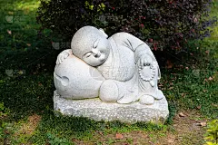 在历史悠久的佛教金山寺，一个小和尚在花园里睡觉的小雕像