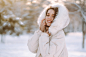 Beautiful woman in winter clothes posing in a snowy park. Young lady walking in a sunny winter day.