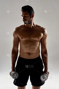 一个年轻的强壮的白人男子的垂直镜头举着重量和看远处，而站在孤立的灰色背景