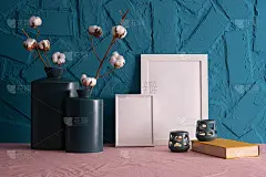 蓝色背景的桌子上放着蓝色花瓶和一株棉花、烛台、一本旧书和相框