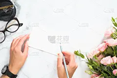 女人的手拿着铅笔和写在空白纸卡片上的模型，在现代家庭办公的办公桌办公文具，玫瑰花束，眼镜，平躺，顶视