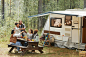 Wide angle view at diverse group of young people clinking beer bottles while enjoying picnic outdoors at campsite with trailer van