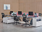 New Aeron Chairs in Carbon finish rolled up to white Layout Studio workstations with salmon colored Pari Screens in contemporary work environment with hard wood walls