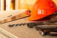 建筑设计图案为橙色塑料头盔，一套钻头和钢丝钳躺在一个浅色的木制背景上