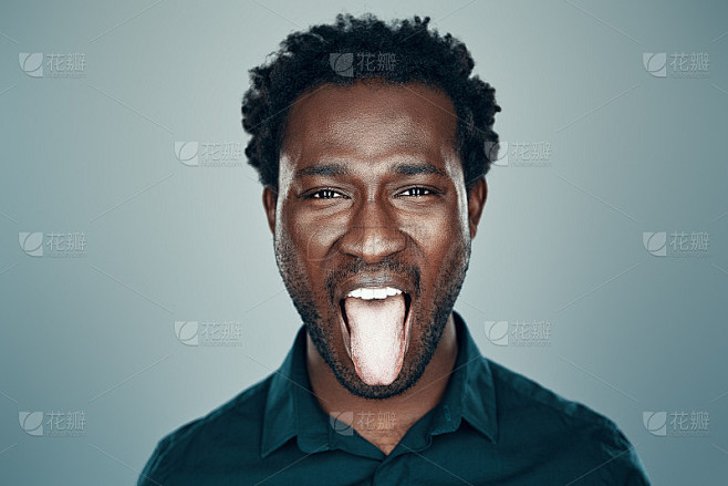 年轻英俊的非洲男子看着镜头，伸出舌头，站在灰色的背景下