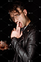 野蛮的人显示中指，同时伸出舌头，拿着一杯威士忌隔离在黑色 