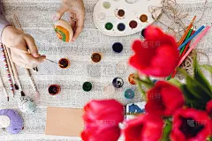手握彩蛋，用颜料、画笔、郁金香花束在质朴的桌子上画彩蛋。平躺，文字空间。孩子装饰复活节彩蛋，准备过节