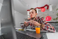 广角拍摄一名年轻白人男子在家里吹生日蜡烛庆祝生日，由于封锁，他和朋友们通过视频集体通话