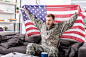兴奋的士兵坐在沙发上，自豪地举着美国国旗欢呼