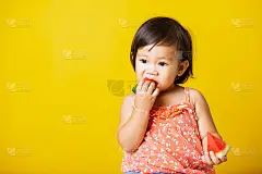 快乐肖像亚洲婴儿或小孩可爱的小女孩迷人的笑微笑穿着t恤玩着切新鲜的西瓜吃，工作室拍摄孤立的黄色背景，