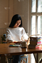 坐在木桌前的一堆书中，一个年轻女子在电脑上打字。