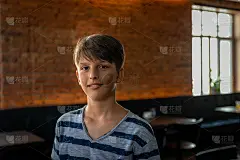 一幅在砖墙前微笑的少年的肖像。它被自然光和背景中的黄光照亮。