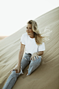 woman in white crew neck t-shirt and blue denim jeans sitting on sand during daytime