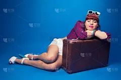 漂亮的海报女郎摆姿势与复古手提箱对抗蓝色