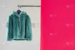 关闭蓬松的绿色人造毛皮大衣衣架与粉红色的壁纸 