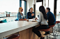 smiling-young-african-american-office-worker-talking-business-wi-colleagues-meeting-around-boardroom-table-146824149