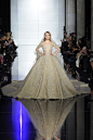 Zuhair Murad Spring 2015 Couture。祖海·慕拉2015春夏高级定系列如千山暮雪，像淡彩的极光。继前几季的洒脱干练、裤装当道之后，该系列回归清丽柔婉的传统，呈现了一场飘飘欲仙的唯美大秀。本季的祖海·慕拉 (Zuhair Murad) 礼服优雅得波澜不惊，然而水乳交融的47套Look实则没有一处雷同，钉珠的排图形、开衩的方式、斗篷和拖尾的处理都各有关窍。此图为最后一身婚纱以《一千零一夜》的传说为灵感，近360度的重工拖尾随着模特缓缓的步伐迤逦而行，裙摆上的花朵以爱与美之名，渐次绽