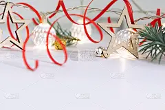 用杉木树枝、木制星星、白色发光球的花环和白色背景上的红丝带组成的圣诞图案。