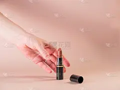 女孩的手从桌上拿起一支黑色外包装的打开的口红。粉状的背景
