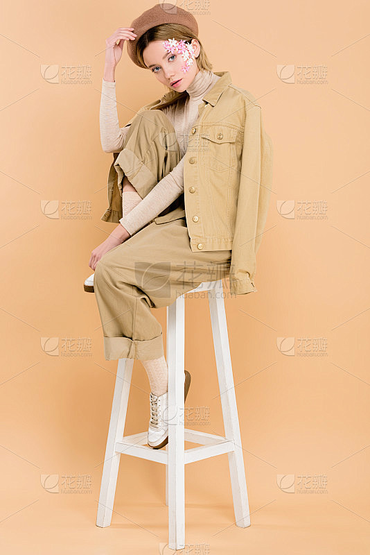 时髦的女孩在贝雷帽坐在椅子上孤立的米色