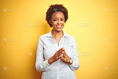 非洲裔美国女商人越过孤立的黄色背景双手合十，十指交叉微笑轻松和愉快。成功和乐观