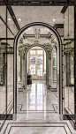 Glam master bathroom features an arched doorway framed by antiqued mirrored walls atop gray marble floors accented with black moldings.