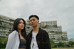 酷酷的亚洲情侣们在寒冷的天气里住在多层楼的宿舍区。严肃的男孩看着相机。关系与爱情概念