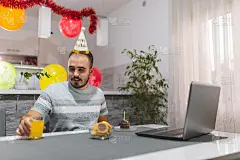 年轻的白人男性正在准备他的生日派对，因为冠状病毒限制，他的朋友们正在他的笔记本电脑上进行集体视频通话