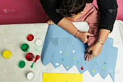 特殊教育的老师和学生穿着长袍，在桌子上用手画着生日花环和涂着丙烯颜料的黄色纸板。塑料工艺疗法。