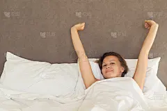 黑发女郎醒来后在床上伸开双手，太阳耀斑。晚上睡个好觉后，女孩带着快乐和放松的表情进入一天。