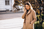 Young woman in beige coat using phone outside the street