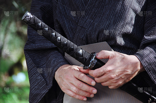 武士的手拿着典型的剑，背景是绿色和树