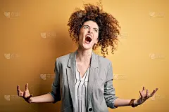 年轻漂亮的女商人，一头卷发，穿一件优雅的外套，疯狂的大喊大叫，挑衅的表情和举起的手臂。挫折的概念。