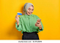Cheerful young Asian woman in a green shirt holding mobile phone and credit card, rejoicing luck on yellow background 库存照片