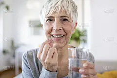 微笑，快乐，健康，50多岁的中年妇女，拿着一杯水，服用膳食补充维生素丸。老年妇女多种抗氧化剂抗衰老美