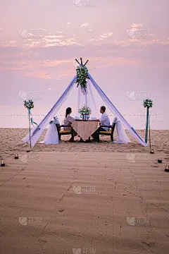 年轻夫妇蜜月晚餐烛光日落在海滩上，男人和女人在海滩晚餐浪漫的设置在泰国日落芭堤雅